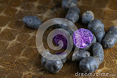 Vitelotte, french purple potatoes sliced in half with a knife on wooden board at rustic kitchen table. Blue variety of popular pot Stock Photo
