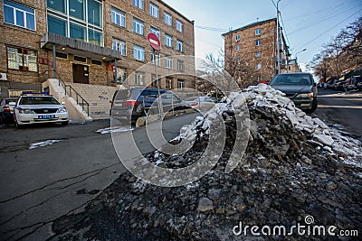 Vladivostok, Russia, 2017 - Dirty street in Vladivostok. Cars are parked in front of large muddy snow drifts on the streets of Editorial Stock Photo