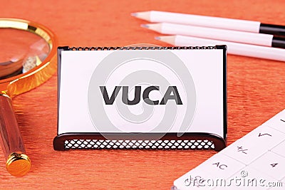 Volatility Uncertainty Complexity Ambiguity. VUCA text on a white business card, close-up in front of an orange background, front Stock Photo
