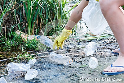 Volunteer boy in blue t shirt picks up dirty plastic bottles in park. Hands in yellow gloves collect garbage, pick up trash Stock Photo