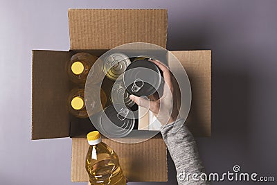 Volunteer hands collecting food into donation box. Top view to cardboard box with grocery products. Donation, charity Stock Photo