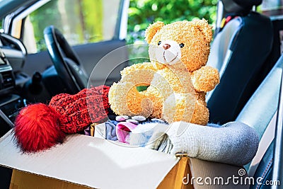 Volunteer provide clothing donation box with used clothes and doll in car to support help for refugee, homeless or poor people in Stock Photo
