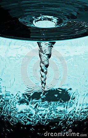 Water glass with rotating column of air, water tube with blue vortex storm of air, decorative kinetic technical sculpture. Stock Photo