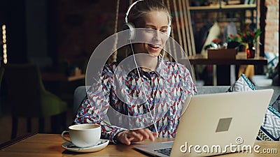 Vrolijke jonge vrouw die in hoofdtelefoons aan muziek luisteren die laptop in koffie met behulp van stock videobeelden Vrolijke jonge vrouw die in hoofdtelefoons aan muziek luisteren die laptop in koffie met behulp van stock videobeelden