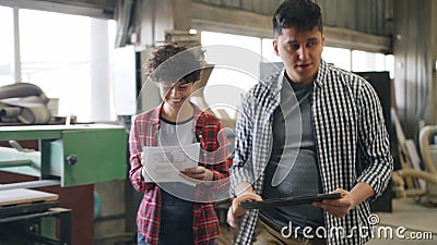 Vrolijke mensen die in houten workshop spreken die met tablet en document documenten lopen stock footage Vrolijke mensen die in houten workshop spreken die met tablet en document documenten lopen stock footage
