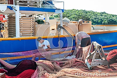 8. 28. 2012. Vrsar. Croatia. Sailors repair the network for fishing, sitting on the shore near the ship Editorial Stock Photo