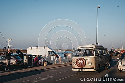 VW Camper van drives past people relaxing by the sea in Wells-next-the-sea, Norfolk, UK Editorial Stock Photo