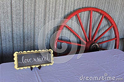 A wagon wheel leaning against the wall of a barn with a sign on a table for a traditional old-fashioned wedding celebration Stock Photo