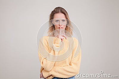 Waist-up portrait go young blond woman showing hush sign with serious face expression. asking to not tell her secret to anyone. Stock Photo