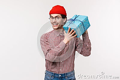 Waist-up portrait happy and excited cute bearded guy trying guess whats inside box, shaking wrapped gift curious what Stock Photo