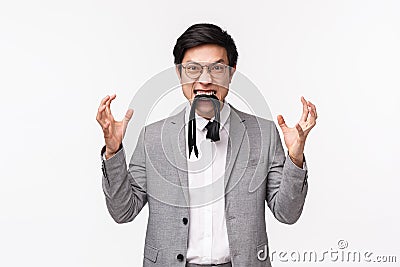 Waist-up portrait of pissed-off, distressed and irritated young asian man eating his own tie and clenching fists Stock Photo