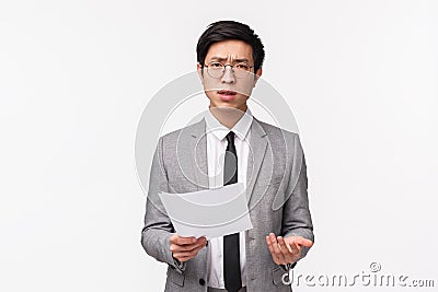 Waist-up portrait of skeptical, serious-looking asian businessman scolding employee for strange bad report, holding Stock Photo