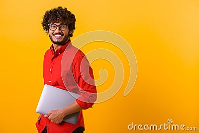 Waist up portrait view of the smiling positive indian man holding laptop in hands and going somewhere. Indoor studio Stock Photo