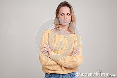 Waist-up portraite of blonde woman with puzzled face expression looks aside with her arms folded. wearing yellow sweater. poses Stock Photo
