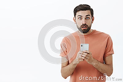 Waist-up shot of amazed and shocked stunned handsome caucasian guy with beard open mouth clueless holding smartphone Stock Photo