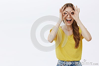 Waist-up shot of funny excited and creative happy caucasian girl with braid in yellow t-shirt making circles over eyes Stock Photo