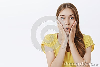 Waist-up shot of impressed speechless good-looking woman in yellow t-shirt holding palms on cheeks folding lips in wow Stock Photo