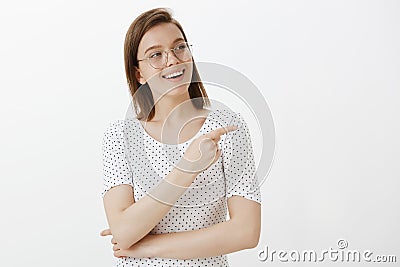 Waist-up shot of pleased and joyful good-looking woman in glasses, smiling broadly, gazing and pointing right with index Stock Photo