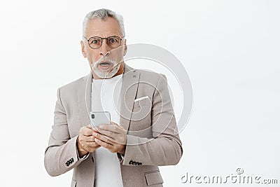 Waist-up shot of shocked senior man in suit and glasses gasping opening mouth from worry and surprise holding smartphone Stock Photo