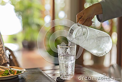 Waiter hand pouring water with ice into glasses on table. Stock Photo