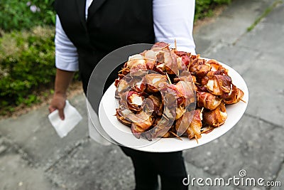 A waiter holding a plate full of bacon wrapped scallops - wedding catering series Stock Photo