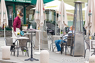 Waiter with a mask disinfects the table of an outdoor bar, cafÃ© or restaurant Editorial Stock Photo