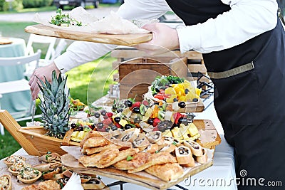 Waiter places food from one plate to another. Catering service. Wedding welcome food. Fruits on skewers and canapes. Stock Photo