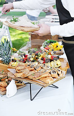 Waiter places food from one plate to another. Catering service. Wedding welcome food. Fruits on skewers and canapes. Stock Photo