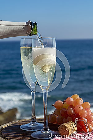 Waiter pouring Champagne, prosecco or cava in two glasses on outside terrace with sea view Stock Photo