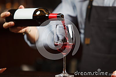 Waiter pouring red wine into wineglass. Sommelier pours alcoholic drink Stock Photo