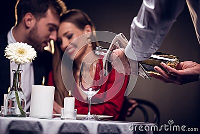 waiter pouring wine while beautiful couple having romantic date in restaurant Stock Photo