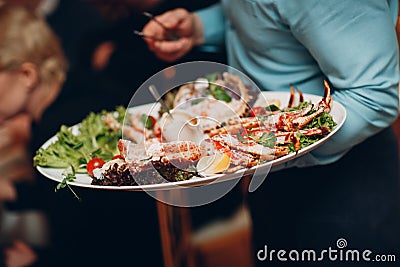 a waiter in a restaurant holds seafood dishes and serves a table catering Concept Healthy food octopus and crabs Stock Photo