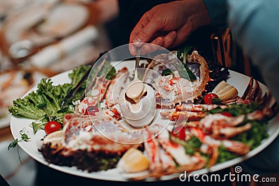 a waiter in a restaurant holds seafood dishes and serves a table catering Concept Healthy food octopus and crabs Stock Photo