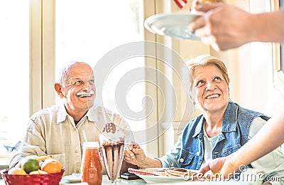 Waiter serving senior retired couple eating cakes at fashion bar Stock Photo