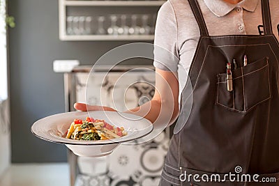 Waiter in uniform hurry to bring customers hot plate of tasty pasta inside modern restaurant Editorial Stock Photo