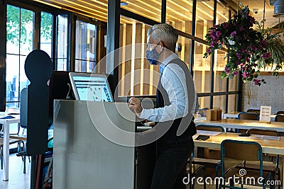 Waiter wearing face mask checking the tables on a counter touch screen. New normal in restaurants Stock Photo