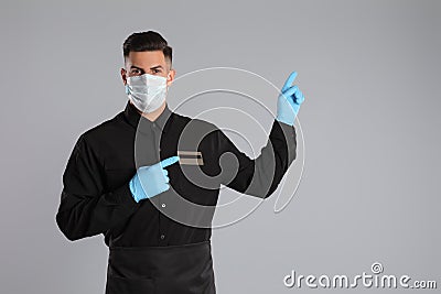 Waiter wearing medical face mask on light grey background Stock Photo
