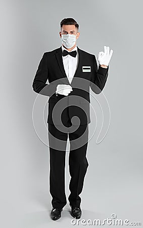 Waiter wearing medical face mask on light grey background Stock Photo