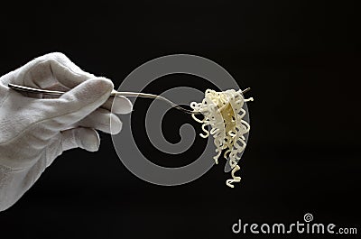 Waiter wearing white gloves holding silver fork and fresh cooked noodles on it, black background Stock Photo
