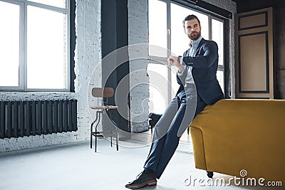 Waiting for a meeting. Serious handsome businessman weared in fashionable suit is looking at watch and waiting Stock Photo