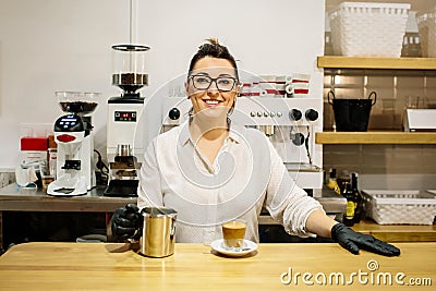 Waitress in a restaurant smiling behind the bar. On the bar a coffee with milk Stock Photo