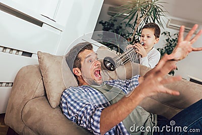 Son wakes up his dad by playing a trumpet Stock Photo