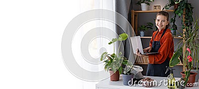 Waking up indoor plants for spring. Teen girl transplants a plant into a new pots at home and uses laptop for her vlog. Stock Photo