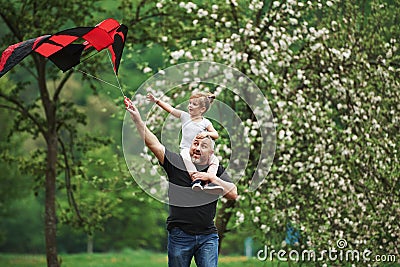 Walking around. Running with red kite. Child sitting on the man`s shoulders. Having fun Stock Photo