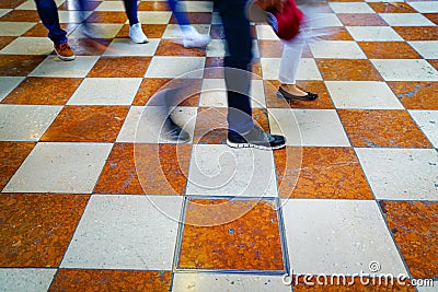 Walking, feet and legs blurred moving across orange and white check patterned marble floor Stock Photo