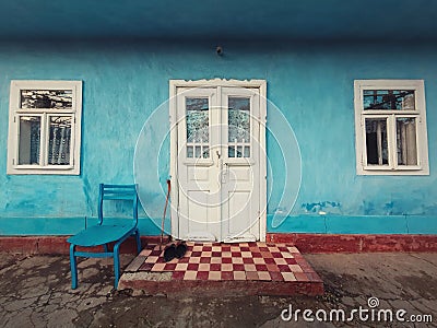 Walking stick, and a pair of old shoes and a chair on the doorstep of an aged house. Traditional rural building facade. Blue lime Stock Photo