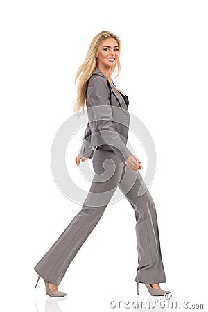Walking Woman In Gray Suit Is Smiling And Looking At Camera Stock Photo