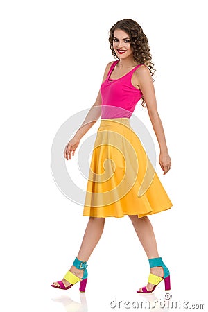 Walking Young Woman In Colorful High Heels, Yellow Skirt And Pink Top Stock Photo