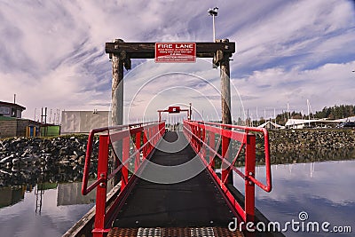 A walkway with bright red railings contrasts against a dramatic sky at a local marina. Editorial Stock Photo