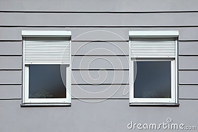 Wall of grey stone building with windows and rolling shutters Stock Photo